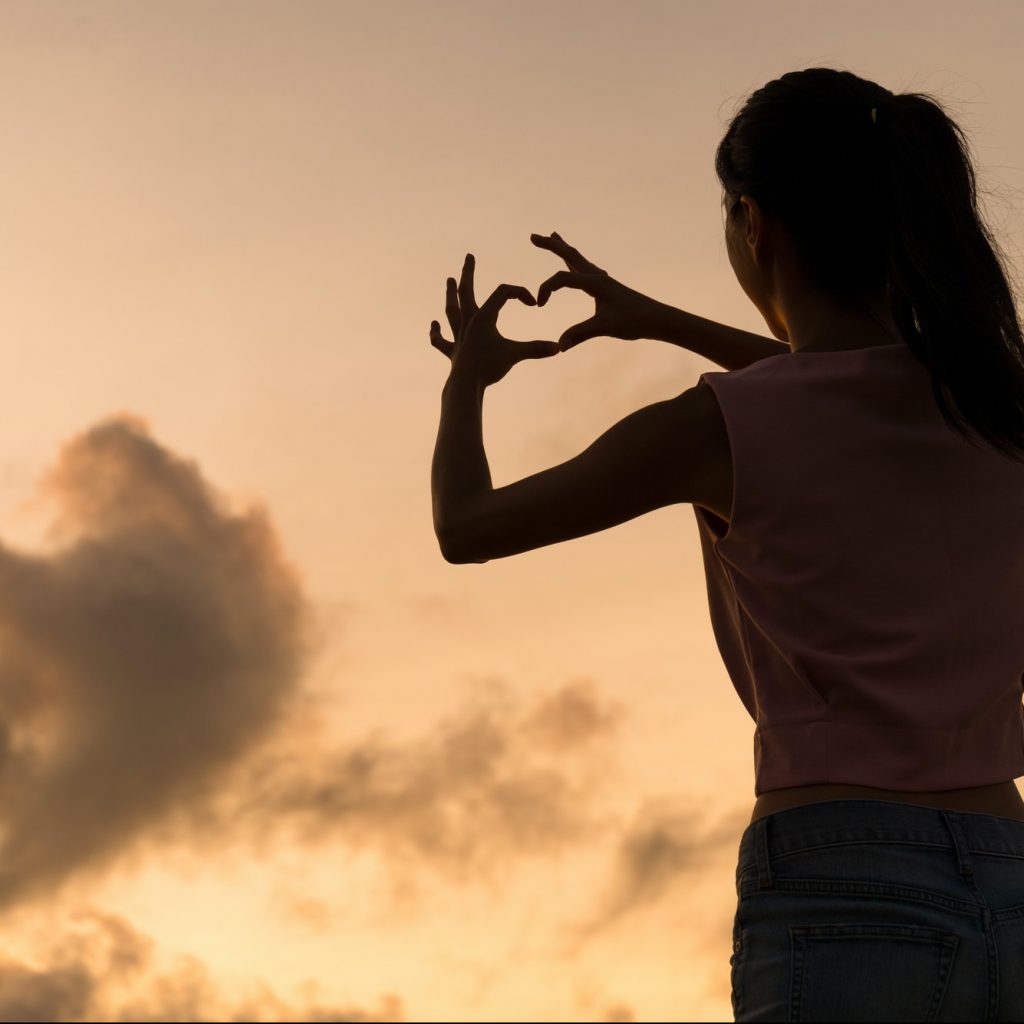 Woman making heart symbol with her hands at sunset